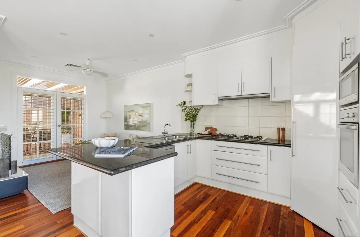 The same Malvern kitchen after the pre-sale repaint and resurface, white gloss doors and drawer fronts around a dark stone benchtop, with the cornices in white