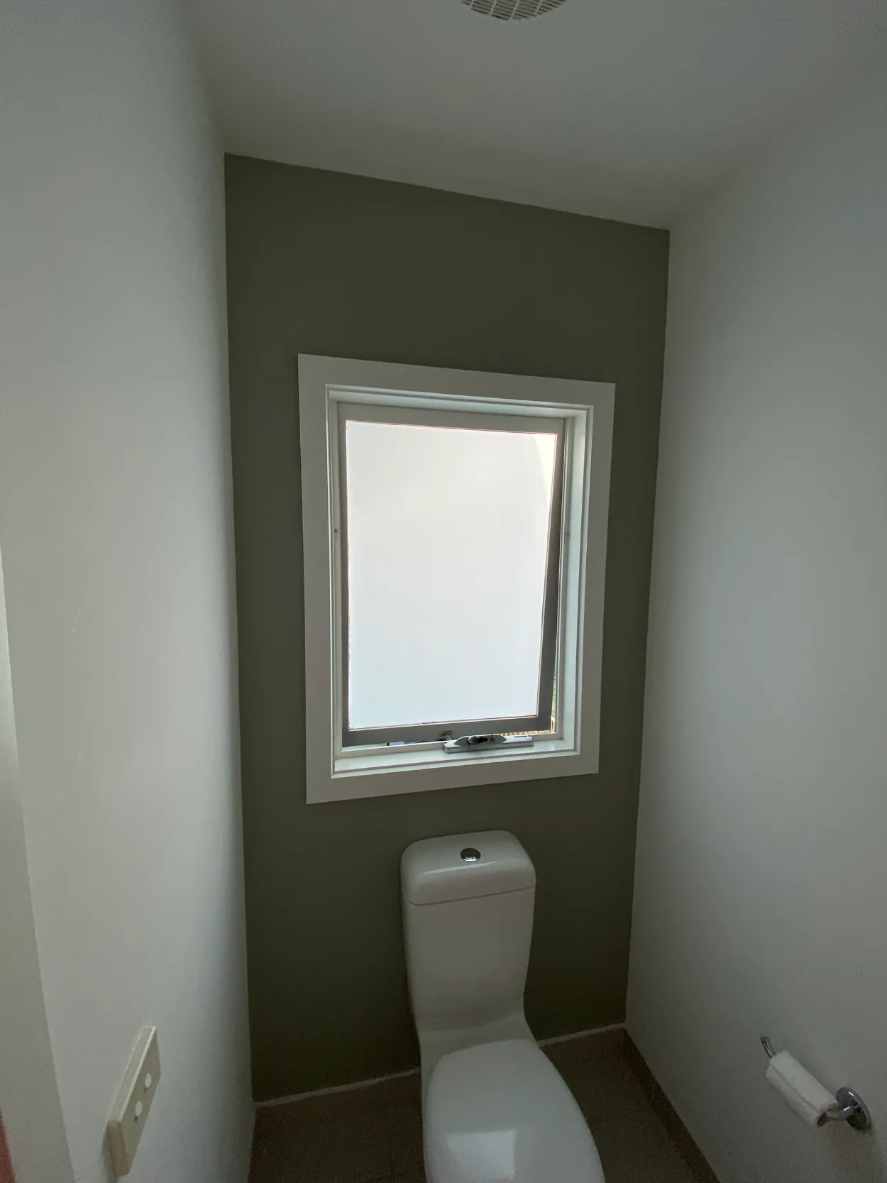 Toilet in a McKinnon home after interior painting, with a sage green feature wall around a white-framed frosted window and white side walls and ceiling