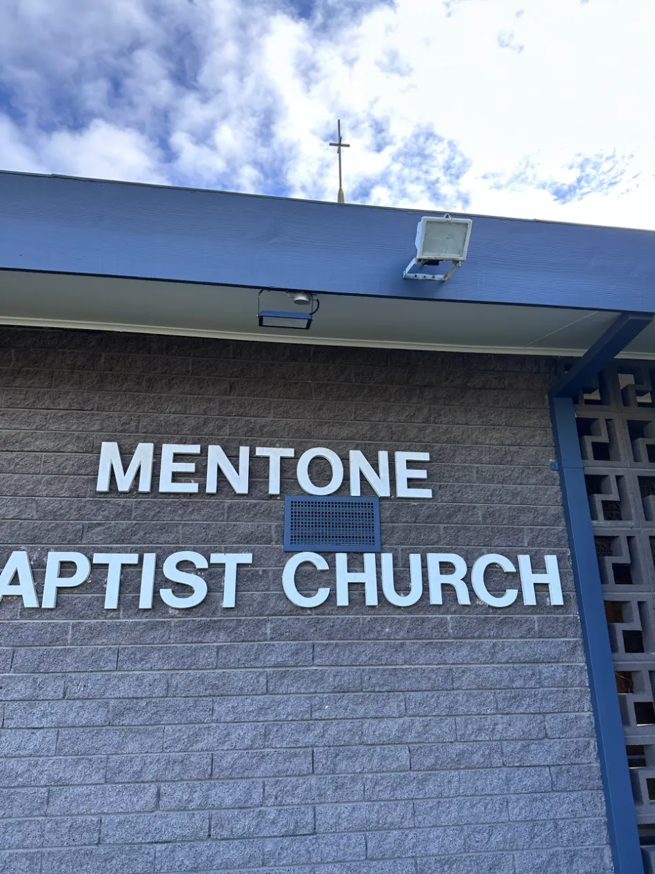 Exterior of Mentone Baptist Church after repainting, showing the blue-grey fascia and grey brick facade with the church's signage and cross