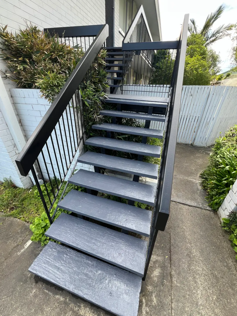 Fire stair in a Mentone apartment building after repainting, charcoal treads and black steel balustrade against a white brick wall