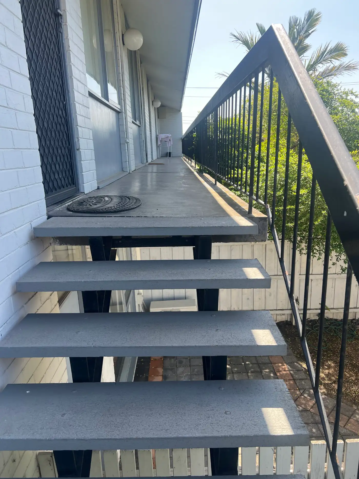 Upper landing and walkway of a Mentone apartment building after repainting, with a charcoal steel balustrade and painted concrete walkway