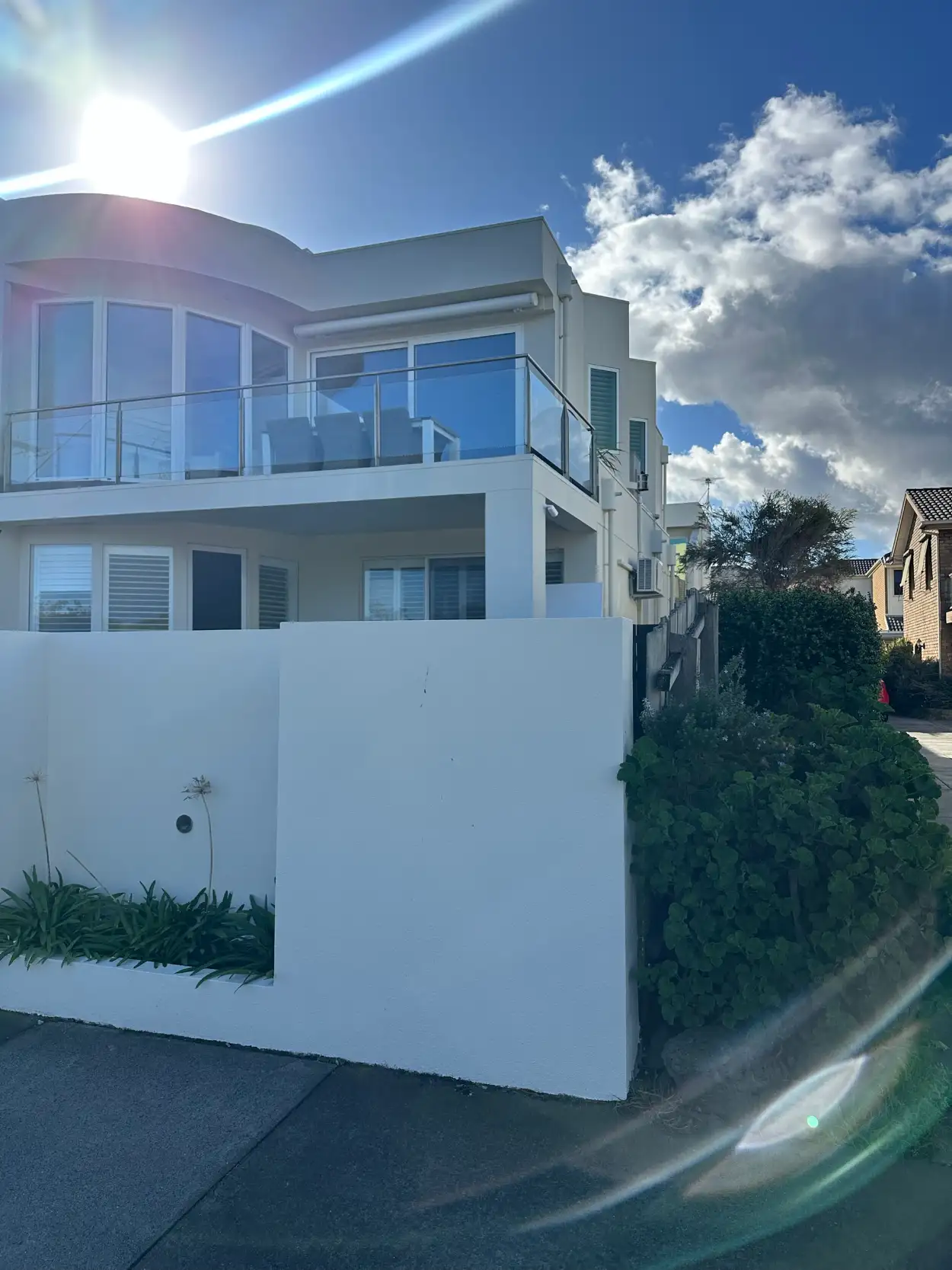 Rendered front wall and garden bed of the same Mordialloc home, finished in white below the two-storey facade and glass balcony