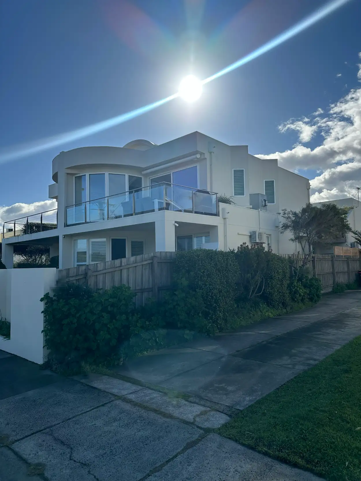 Two-storey rendered home in Mordialloc near the bay after exterior painting, with a curved upper wall and glass balcony in off-white