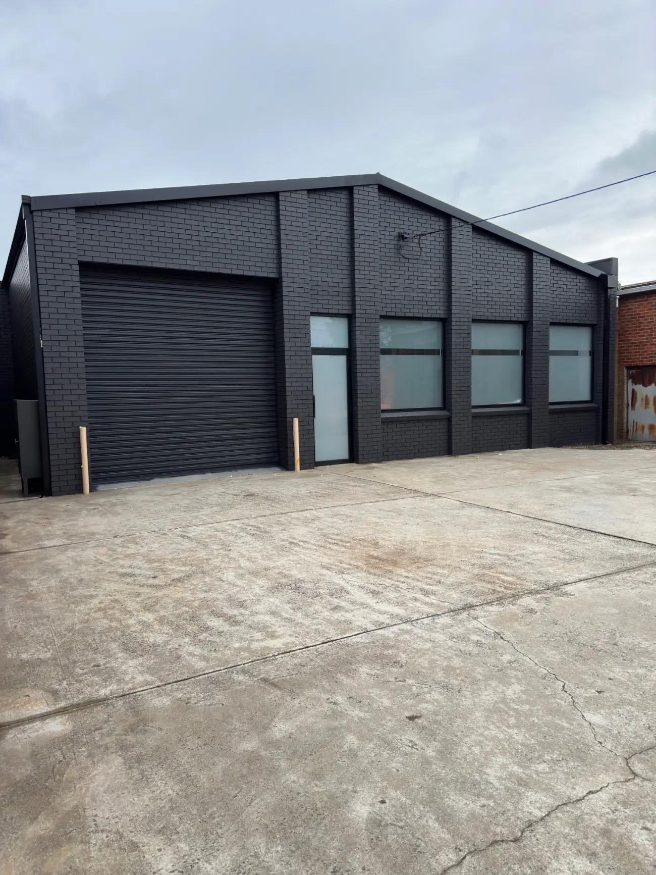 The same Mordialloc commercial warehouse after painting, with the brickwork, roller door and trim all finished in charcoal