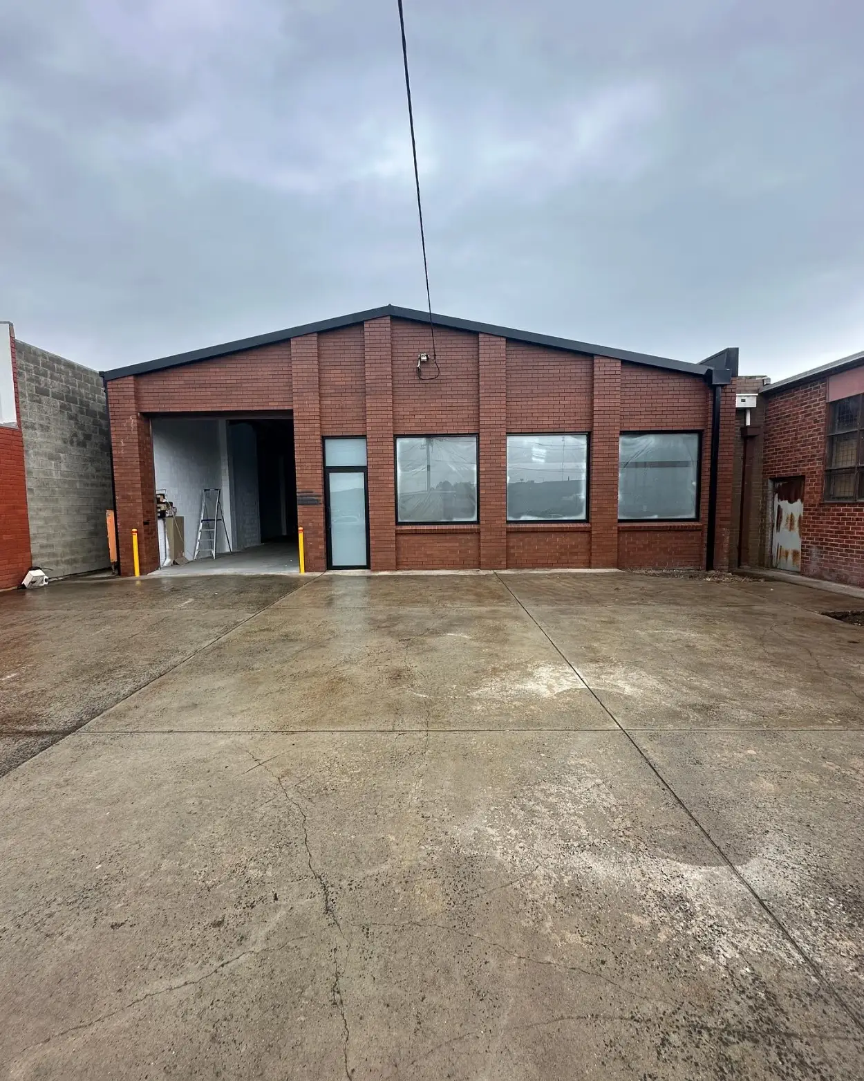 Commercial warehouse in Mordialloc before painting, in red face brick with black roof trim and a roller door opening onto a concrete forecourt