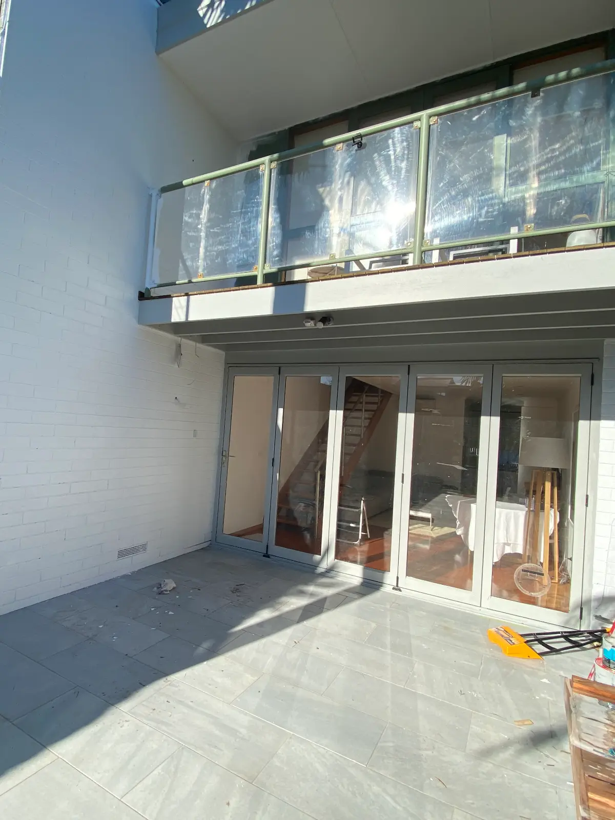 Upper balcony and glass balustrade above the bifold doors of a Mordialloc townhouse courtyard, the glass still covered in protective film during the repaint