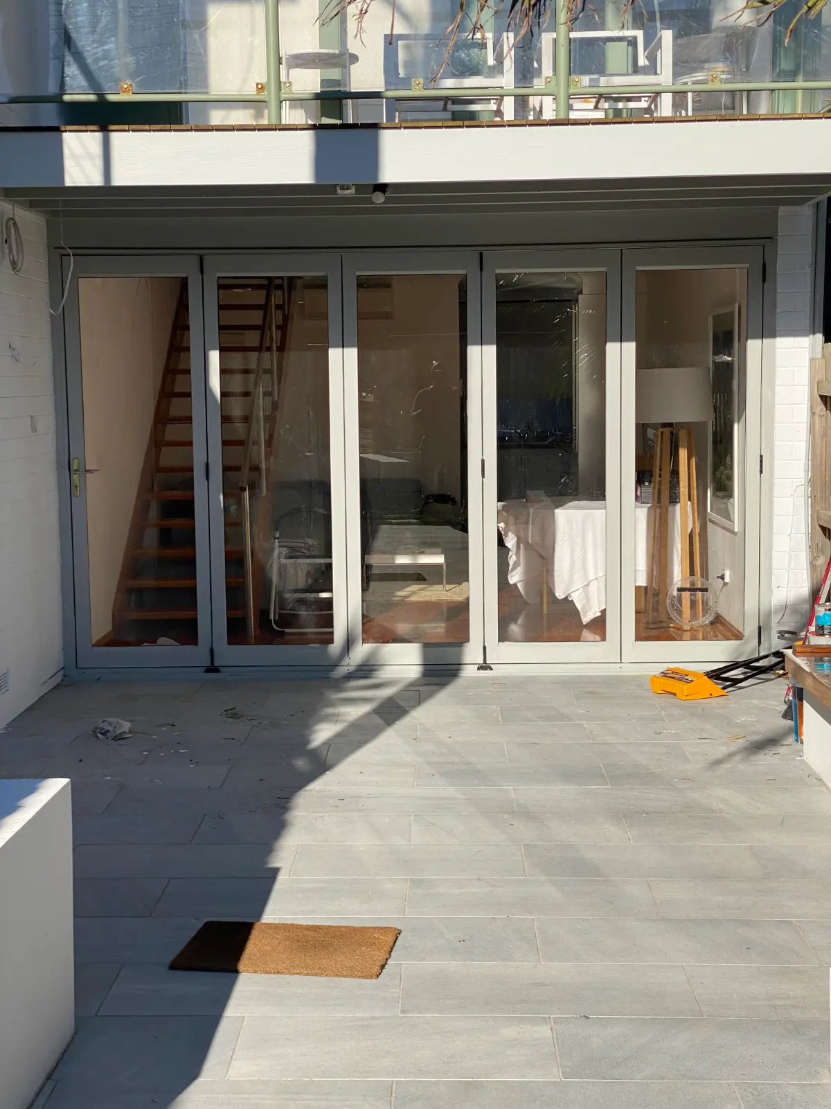 Freshly painted grey-green bifold door frames in the courtyard of a Mordialloc townhouse, with the interior under dust sheets behind the glass