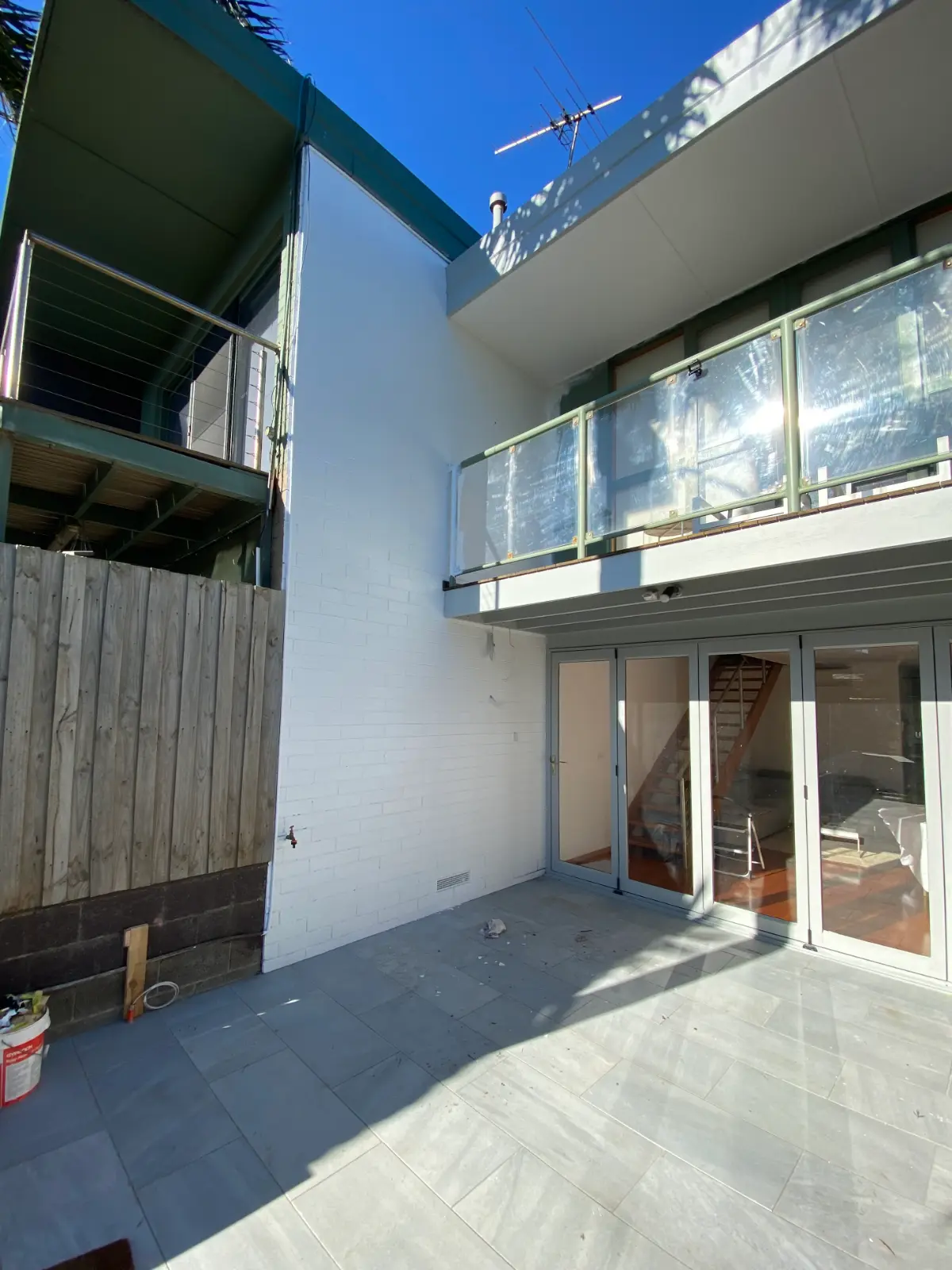 Double-height painted brickwork in the courtyard of a Mordialloc townhouse, white brick meeting a timber boundary fence, with a glass balustrade balcony above