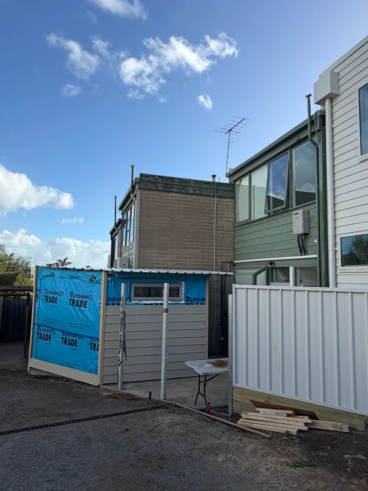 Rear of a Mordialloc property before painting, with brown brick, green weatherboard and a new outbuilding still in building wrap