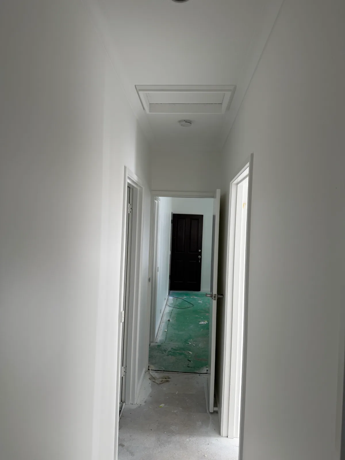 Hallway of a vacant Mordialloc rental after an interior repaint, with white walls, ceiling, manhole and door frames leading to a dark front door