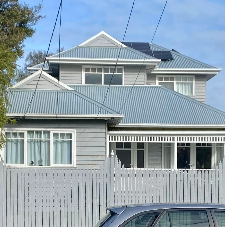 Weatherboard Mordialloc home in pale grey with a grey roof before repainting, behind a white picket fence