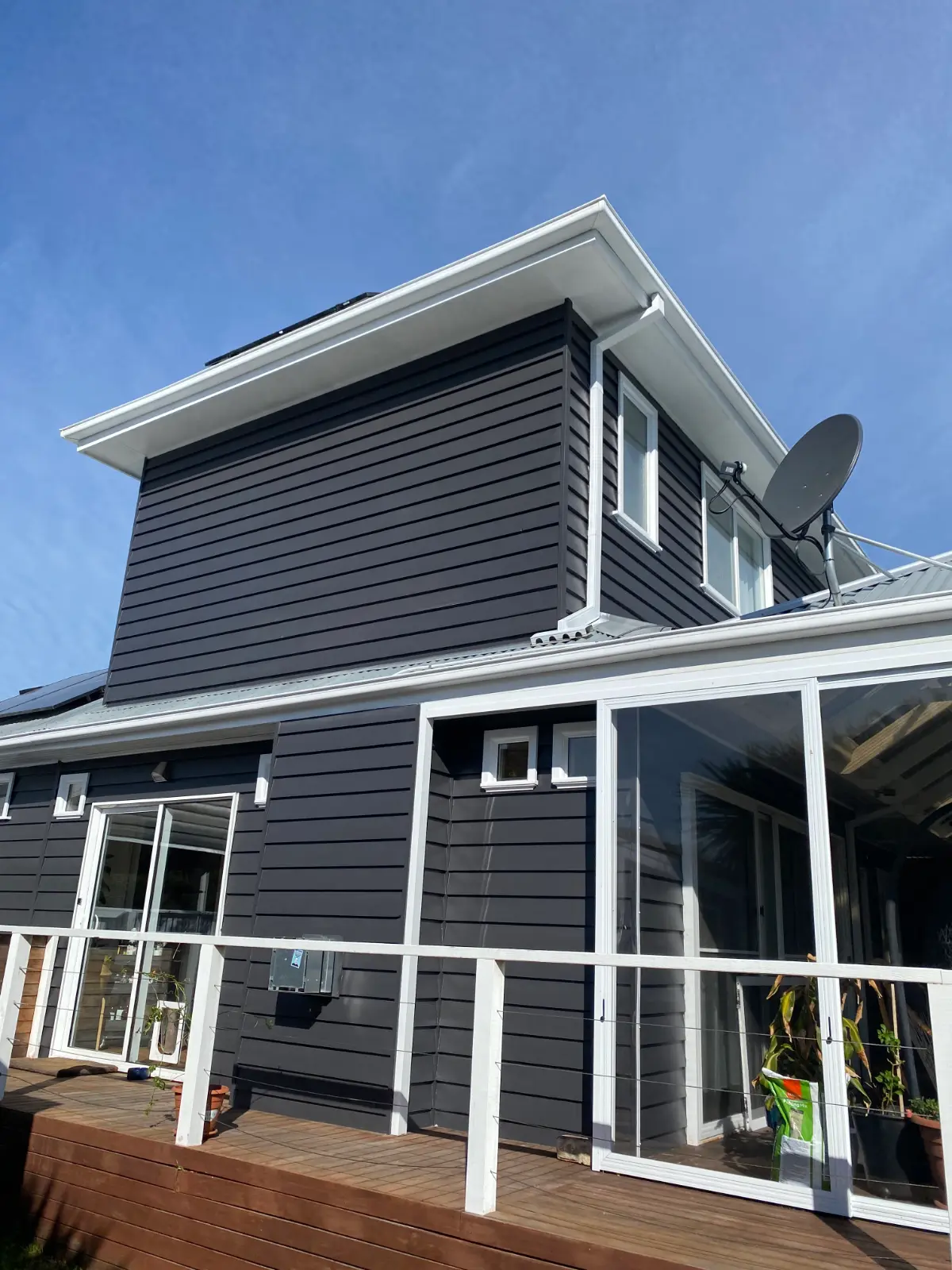 Rear elevation of the same Mordialloc home after repainting, charcoal weatherboard and white trim above a timber deck