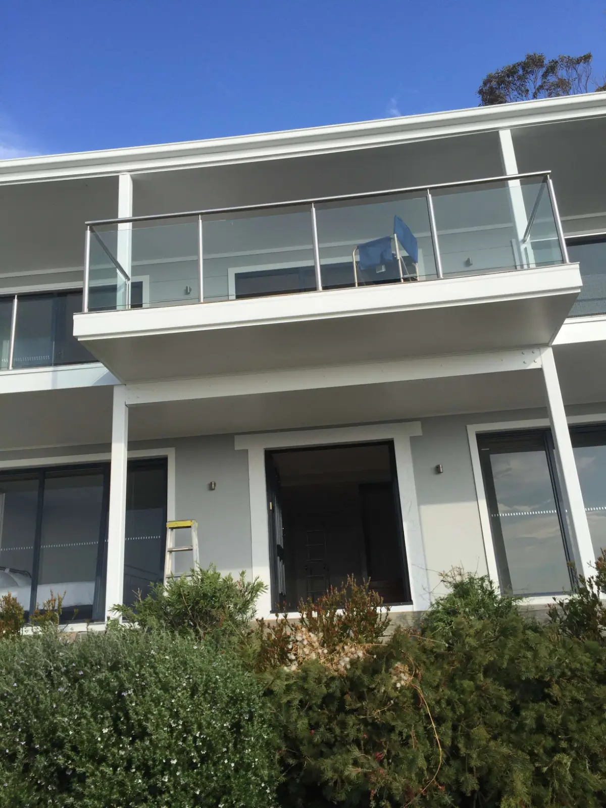 Upper balcony and glass balustrade of a Mount Martha home after repainting, white beams and posts against grey walls