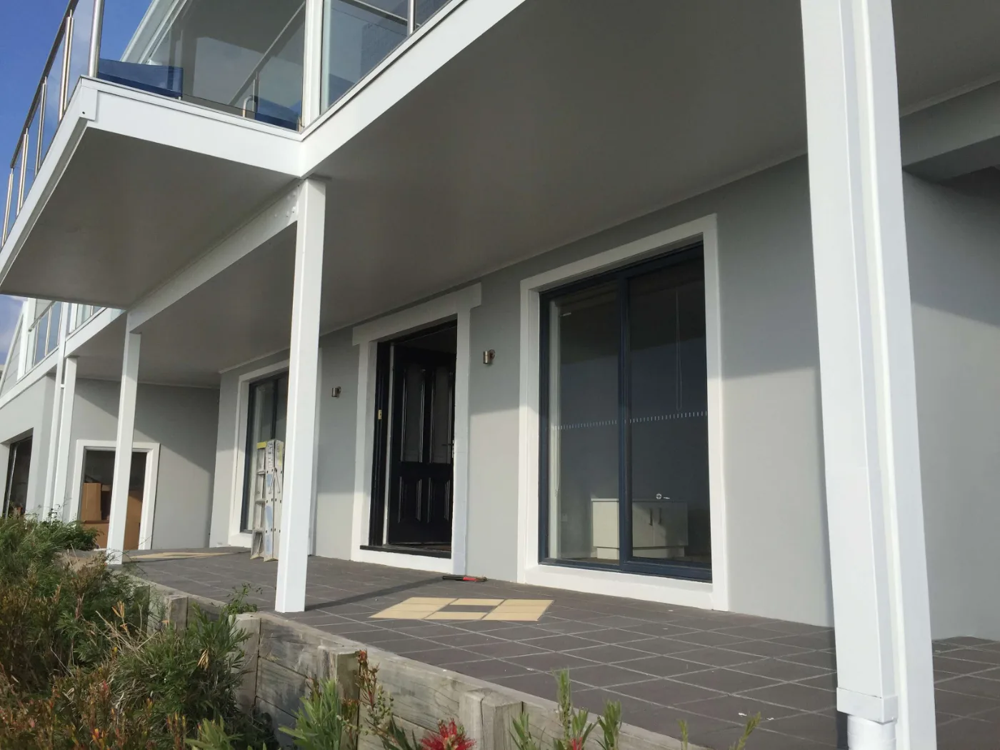 Entry elevation of a Mount Martha home after an exterior repaint, with grey walls, white posts and beams and a black front door