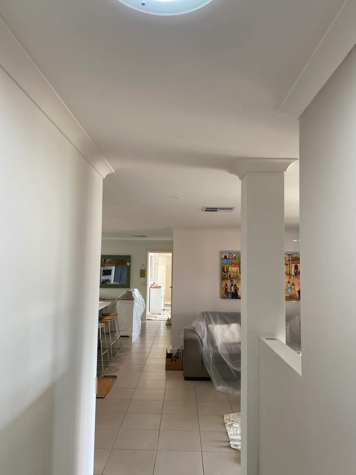 Hallway of a Mount Martha home looking through to the kitchen and living area after an interior repaint, with white ceilings, walls, cornices and a square column with corbels, and furniture still under plastic