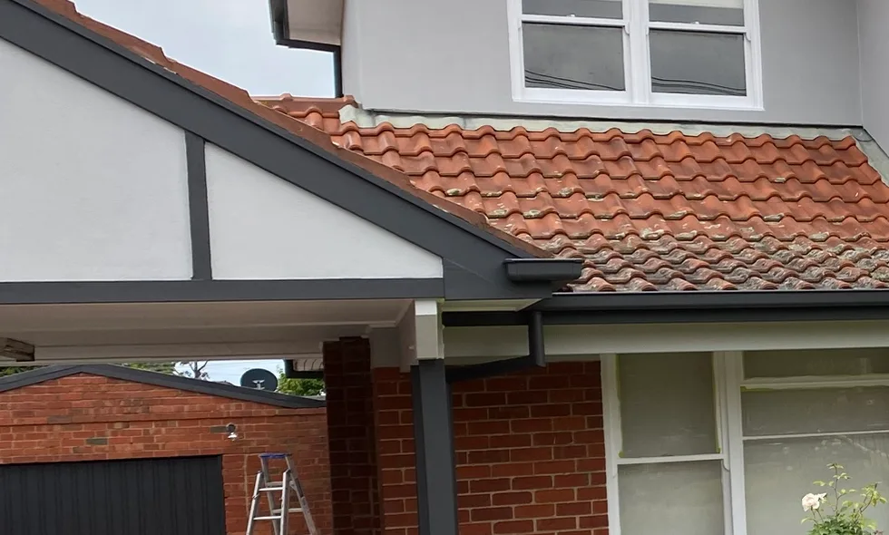 Carport gable on the same Murrumbeena exterior repaint, with charcoal battens, barge board, fascia, gutter and downpipe set against pale render, original red brick and a terracotta tile roof