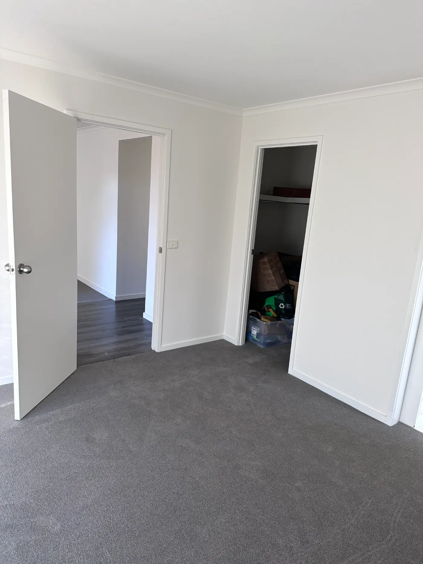 Bedroom in a Narre Warren home after repainting, with white walls, ceiling and trim above grey carpet, and a built-in robe beside a doorway through to the hallway