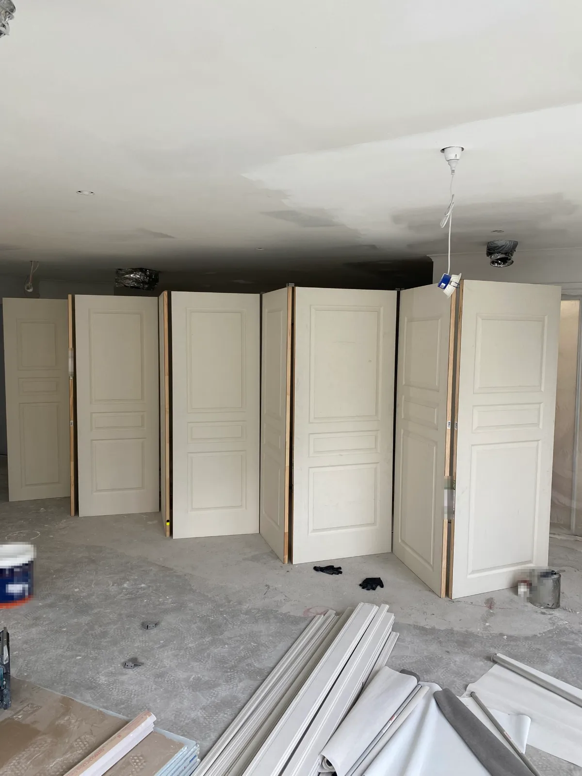 The same run of three-panel doors in the Narre Warren build seen from the other end of the room, stood upright on a concrete slab with architraves stacked in the foreground