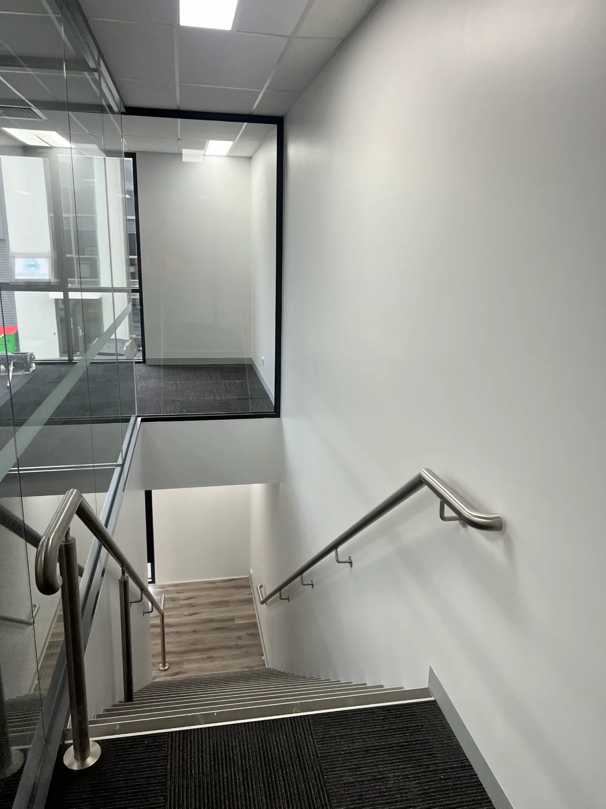 Stairwell in a two-level Chadstone office fitout painted by Jetblack Painting, with cut-in edges running against a glazed partition and stainless handrails