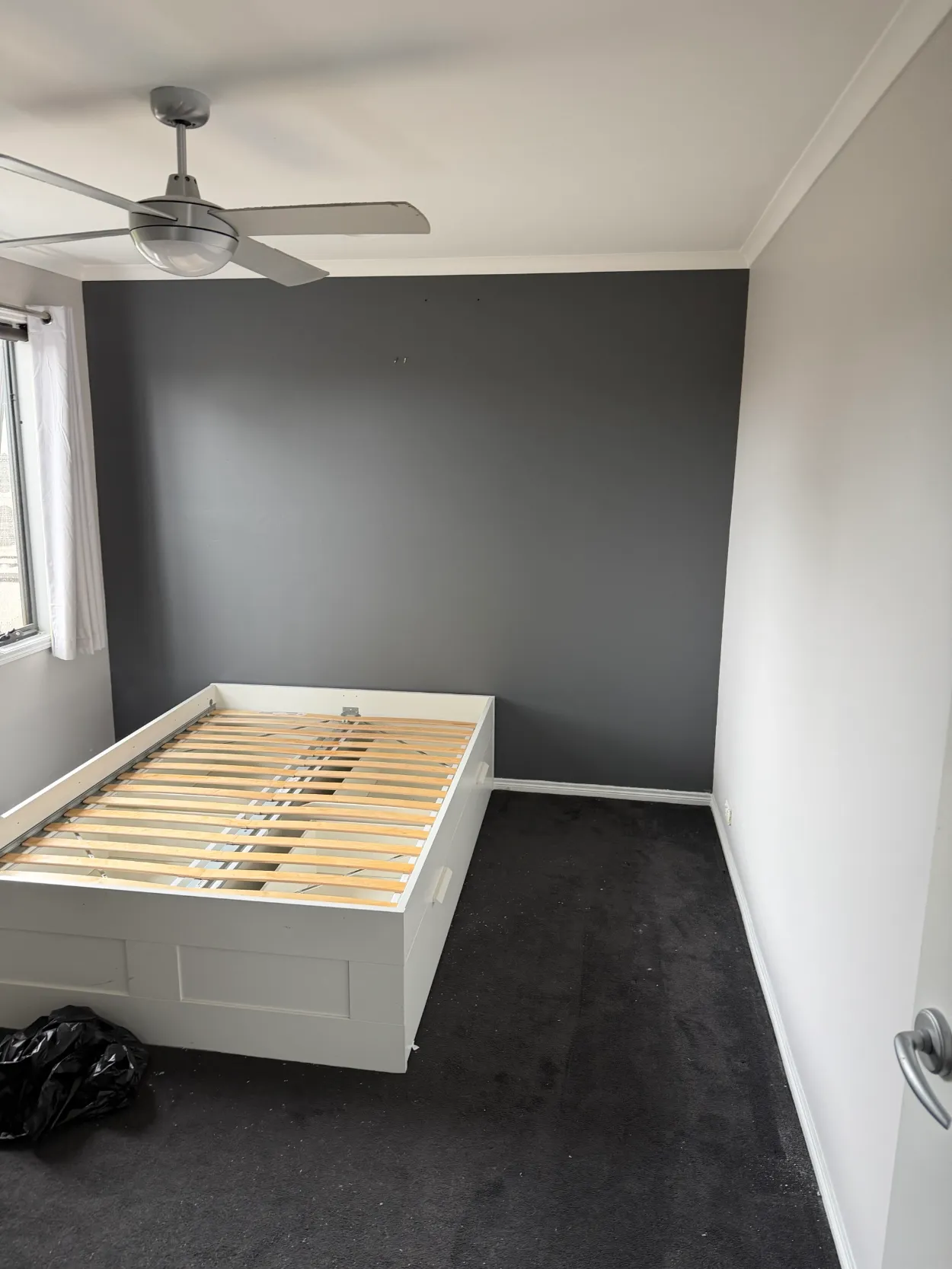 Bedroom in a two-storey Parkdale home, from an interior repaint, with a darker feature wall behind the bed, lighter side walls, white ceiling, cornice and skirting, and a ceiling fan