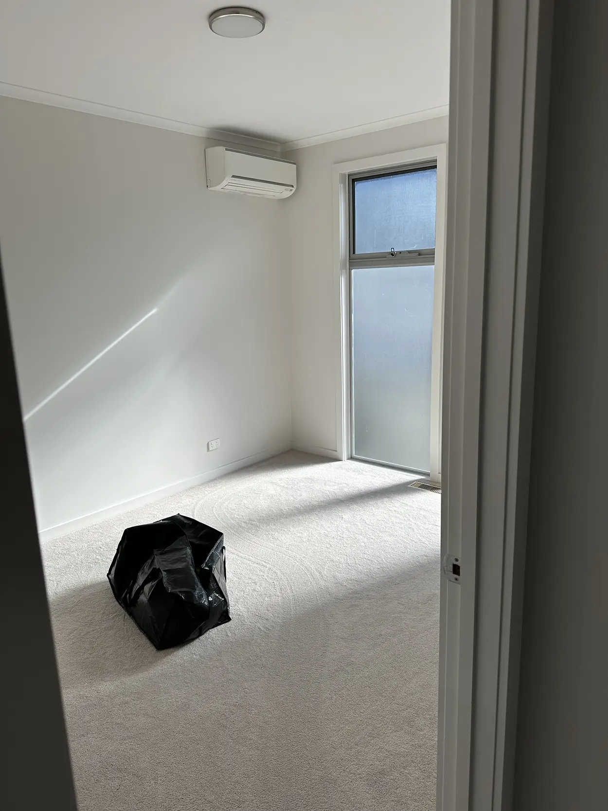 Finished bedroom in Parkdale with white walls, ceiling, cornice and window frame, a split-system air conditioner and a tall frosted window