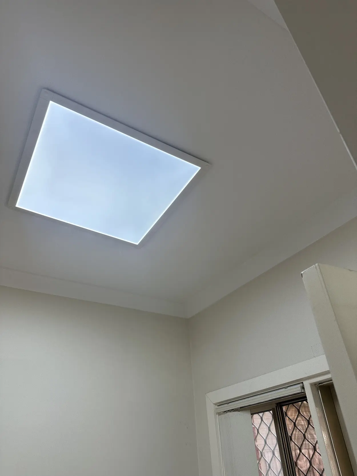 Painted ceiling and cornice in a Parkdale home around a square LED panel light, with the top of a window and door frame below