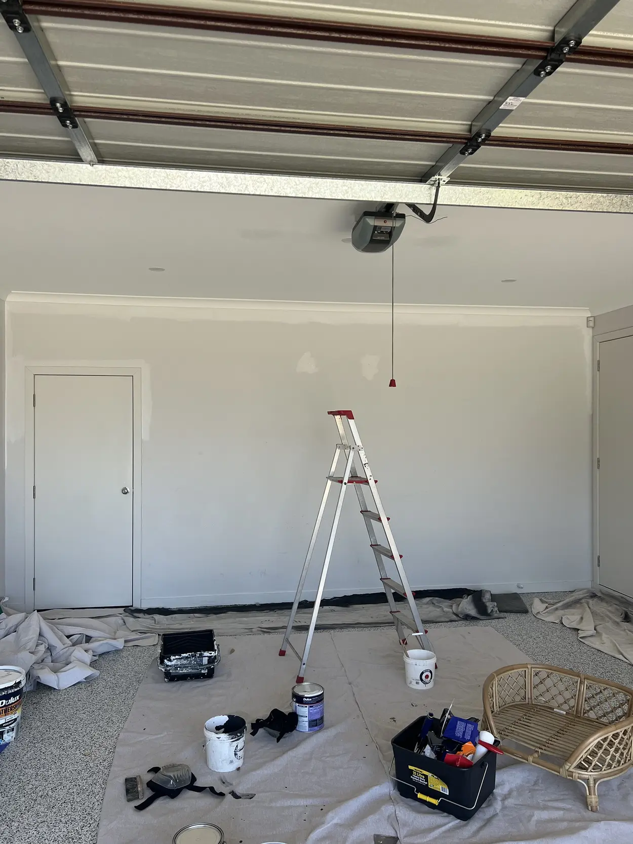 Double garage in Parkdale mid-repaint, with filled patches showing on the back wall, drop sheets across the floor, a stepladder and paint tins
