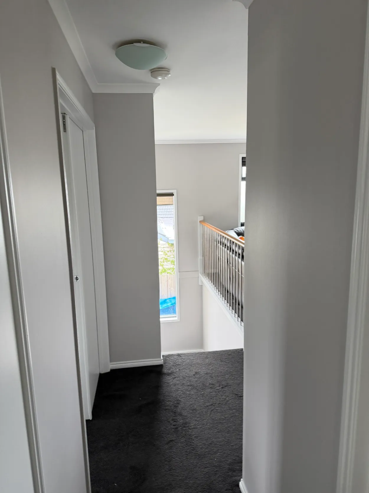 Hallway in a two-storey Parkdale home, from an interior repaint, with grey walls, white door frames, skirting and cornice, looking toward the stairwell window and balustrade