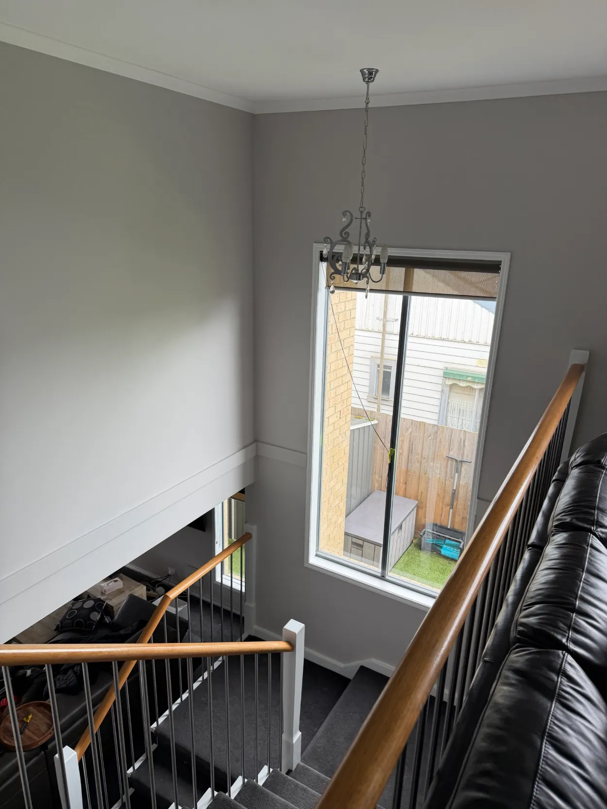 Double-height stairwell in a two-storey Parkdale home, from an interior repaint, with grey walls, white cornice, window frame and stair stringer, a pendant light and a timber handrail with steel balusters