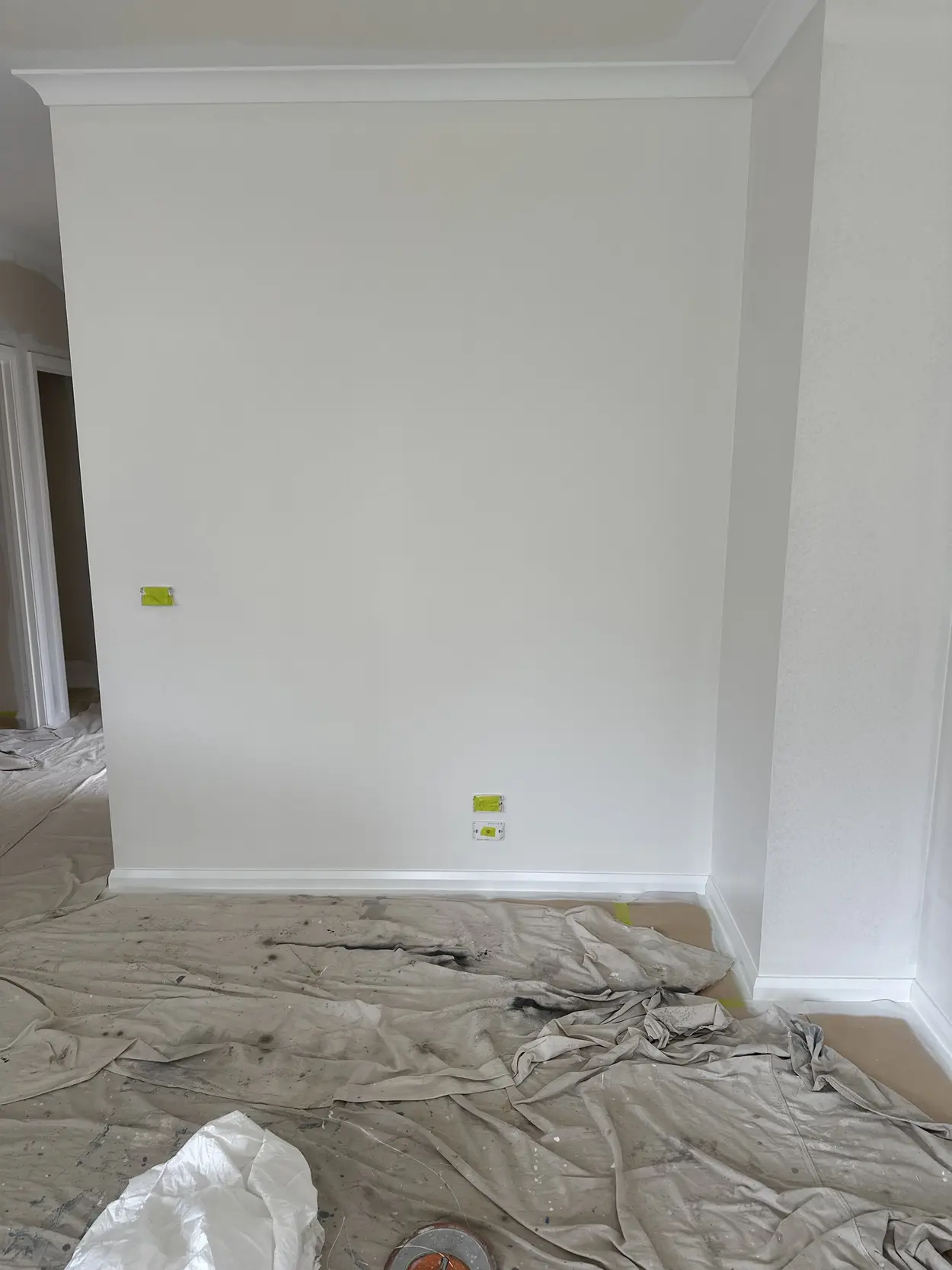 Freshly painted white wall in a Parkdale home with the power point and switch plates taped over, white skirting and cornice, and drop sheets on the floor