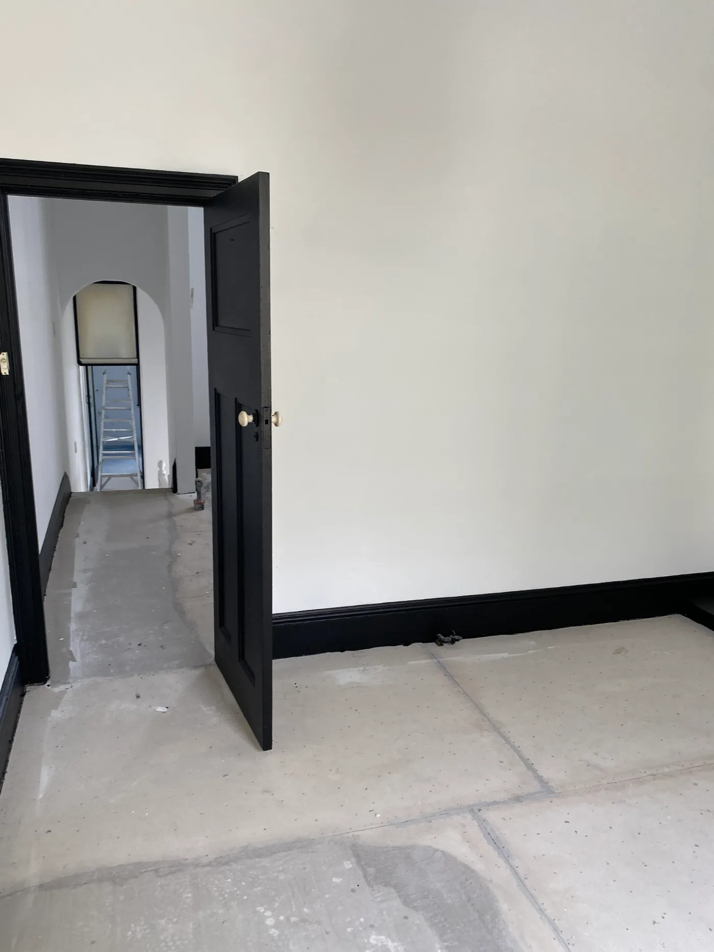 Room in a Prahran property after painting, with white walls and ceiling against a black panelled door, black architraves and black skirting, floor protection still down