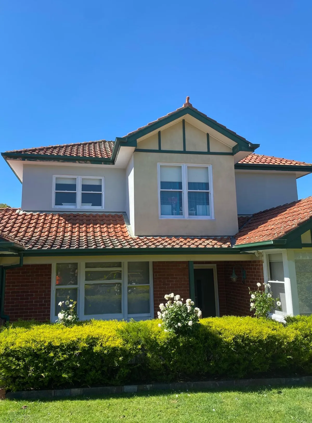 Two-storey home after an exterior repaint, with dark green picked out through the gable strapping, fascias, gutters and downpipes above a red brick ground floor and a terracotta tile roof