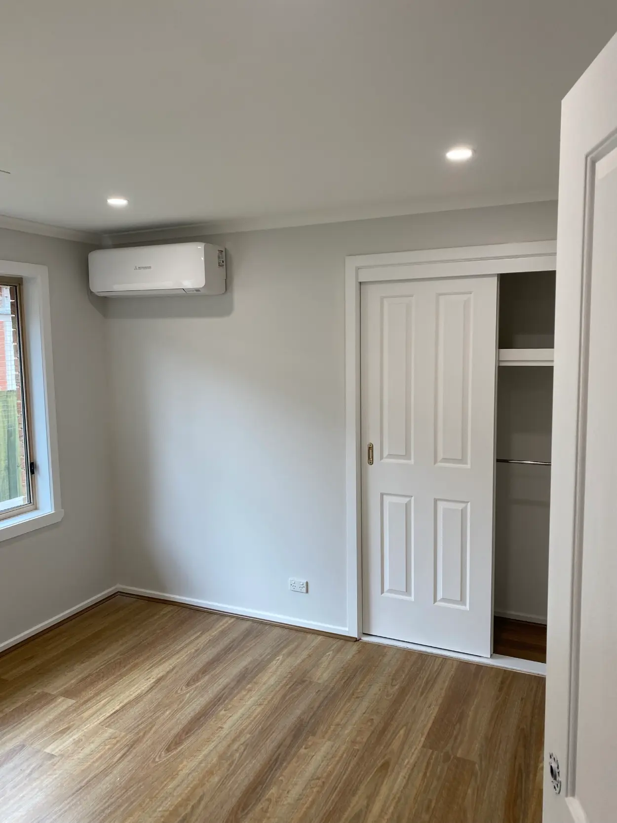 Bedroom in a Rowville home after repainting, with grey walls, a white built-in robe with sliding doors, a wall-mounted split system and timber-look flooring