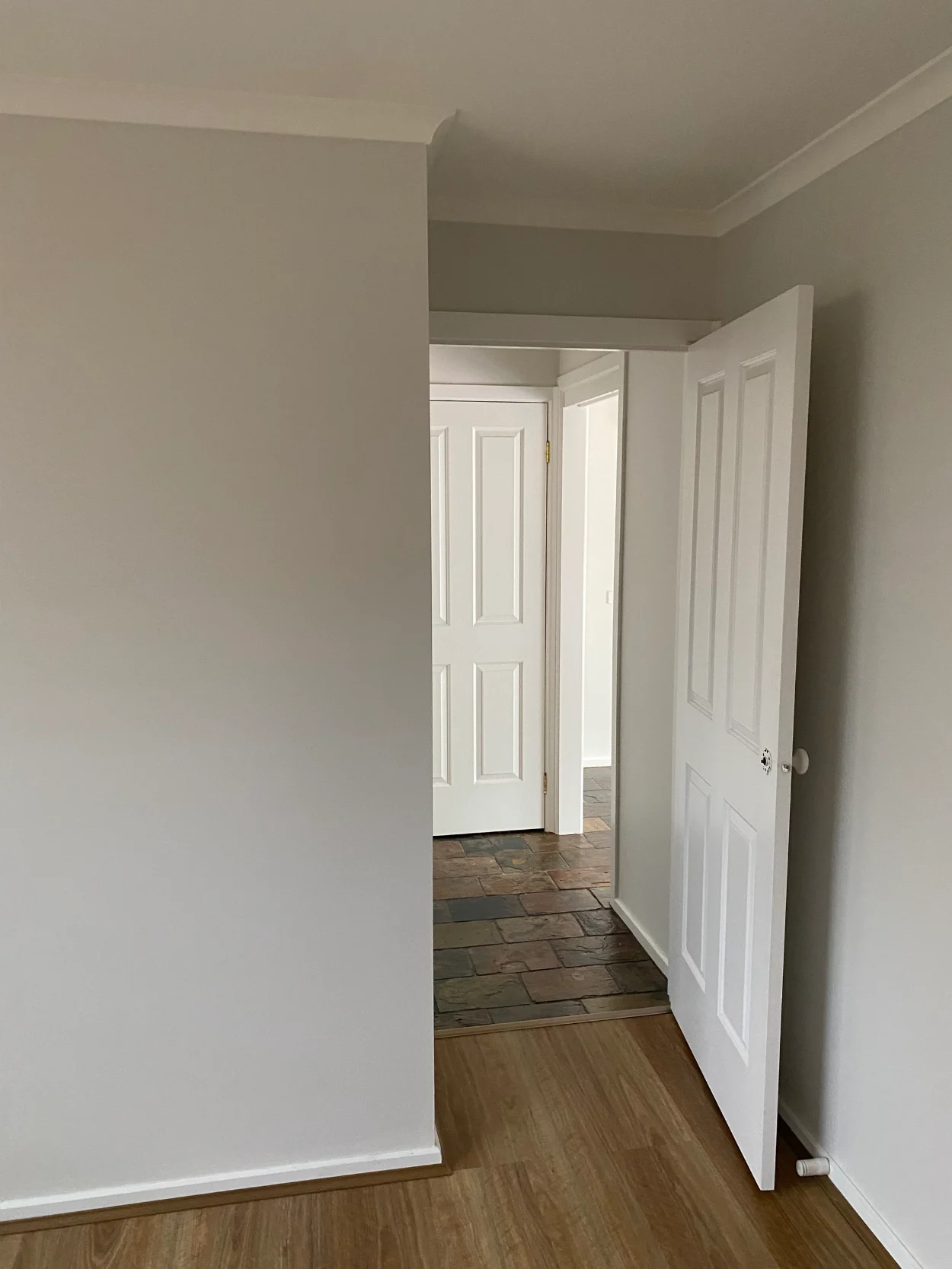 Doorway in a Rowville home after repainting, looking through a grey-walled room to a hallway with white four-panel doors, white architraves and a slate floor meeting timber-look boards