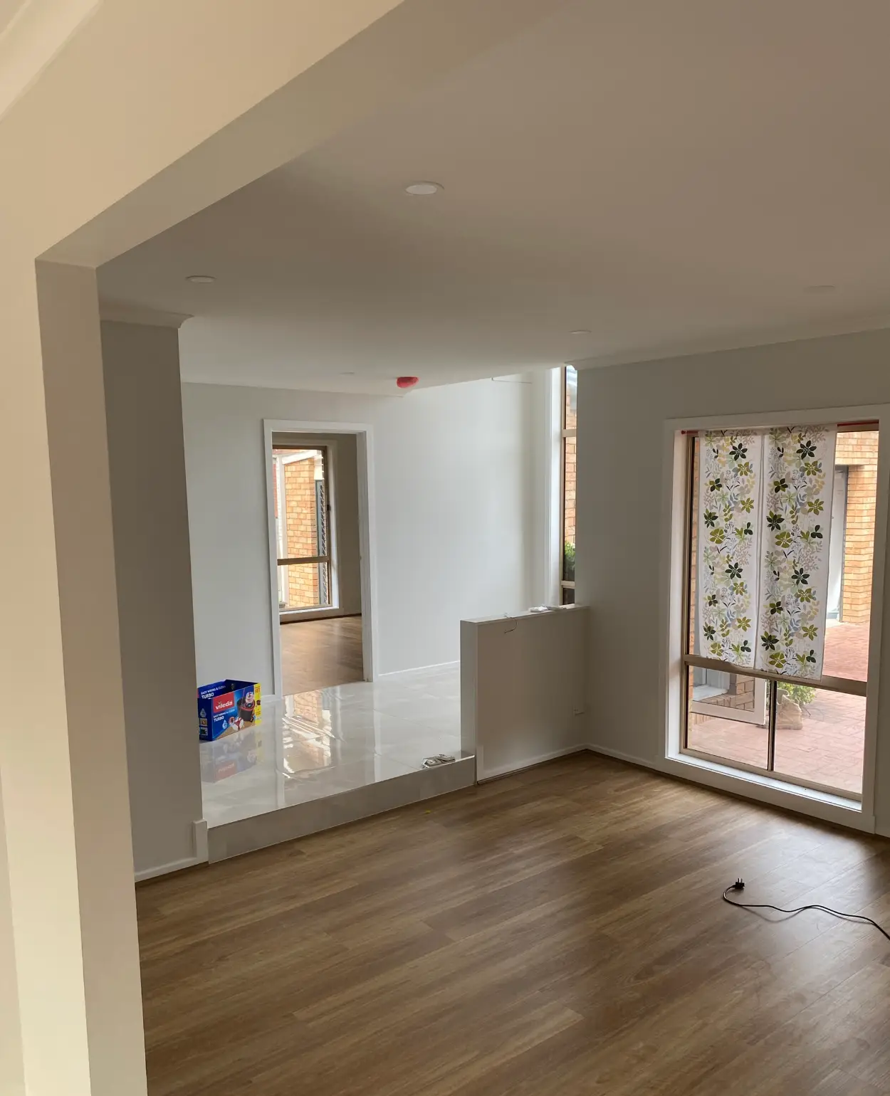 Living and dining area of a Rowville home after repainting, with white ceilings, two wall tones, timber-look flooring and large windows looking onto a brick courtyard