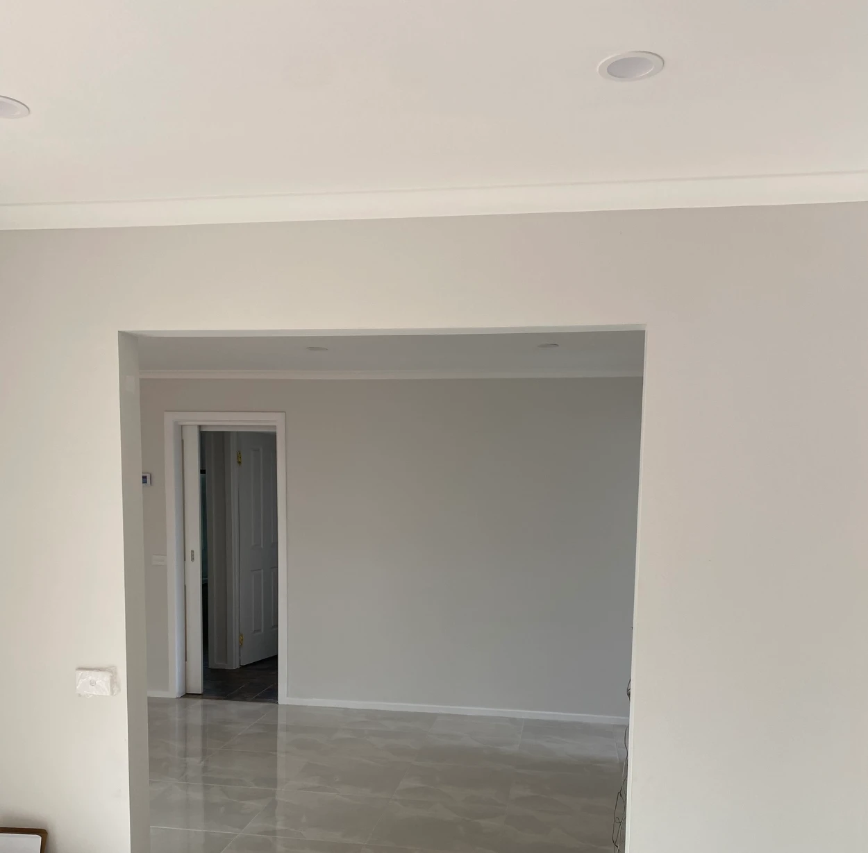 Wide square-set opening between two repainted rooms in a Rowville home, warm white on the near wall and cooler grey beyond, above large-format gloss floor tiles