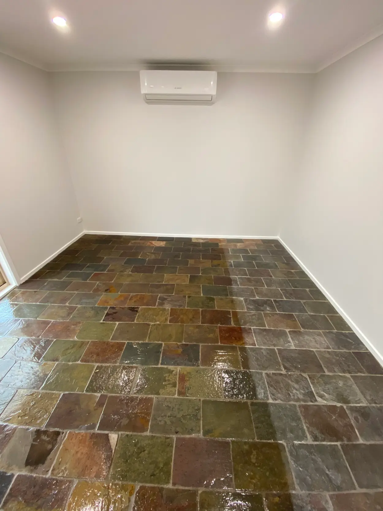 Empty room in a Rowville home after repainting, with white walls and ceiling, a wall-mounted split system and downlights above an original multicoloured slate flagstone floor