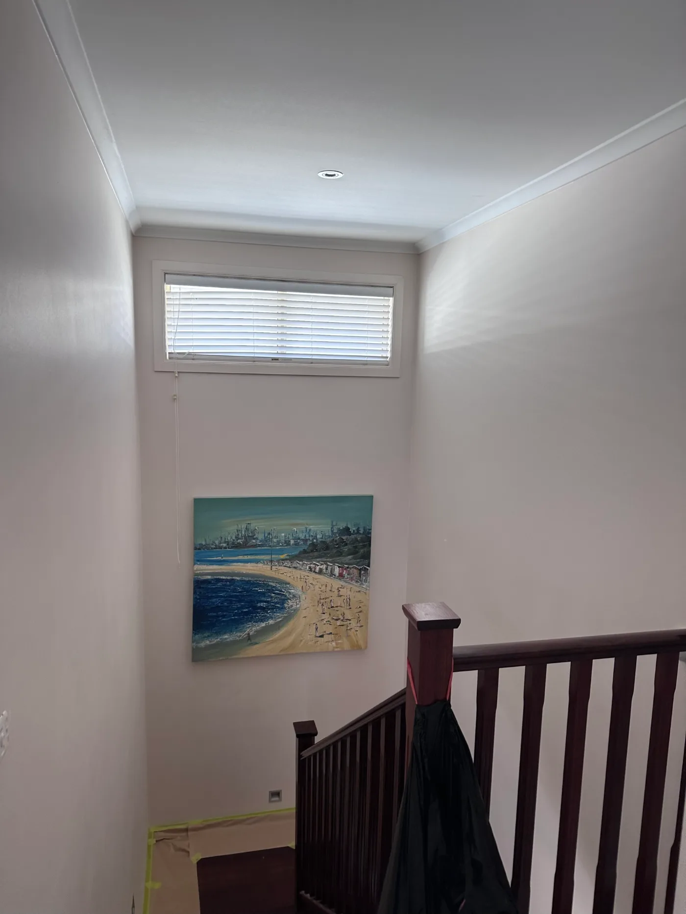 Stair landing in a Sandringham home during repainting, with masking and floor protection in place below a high window and a dark timber balustrade