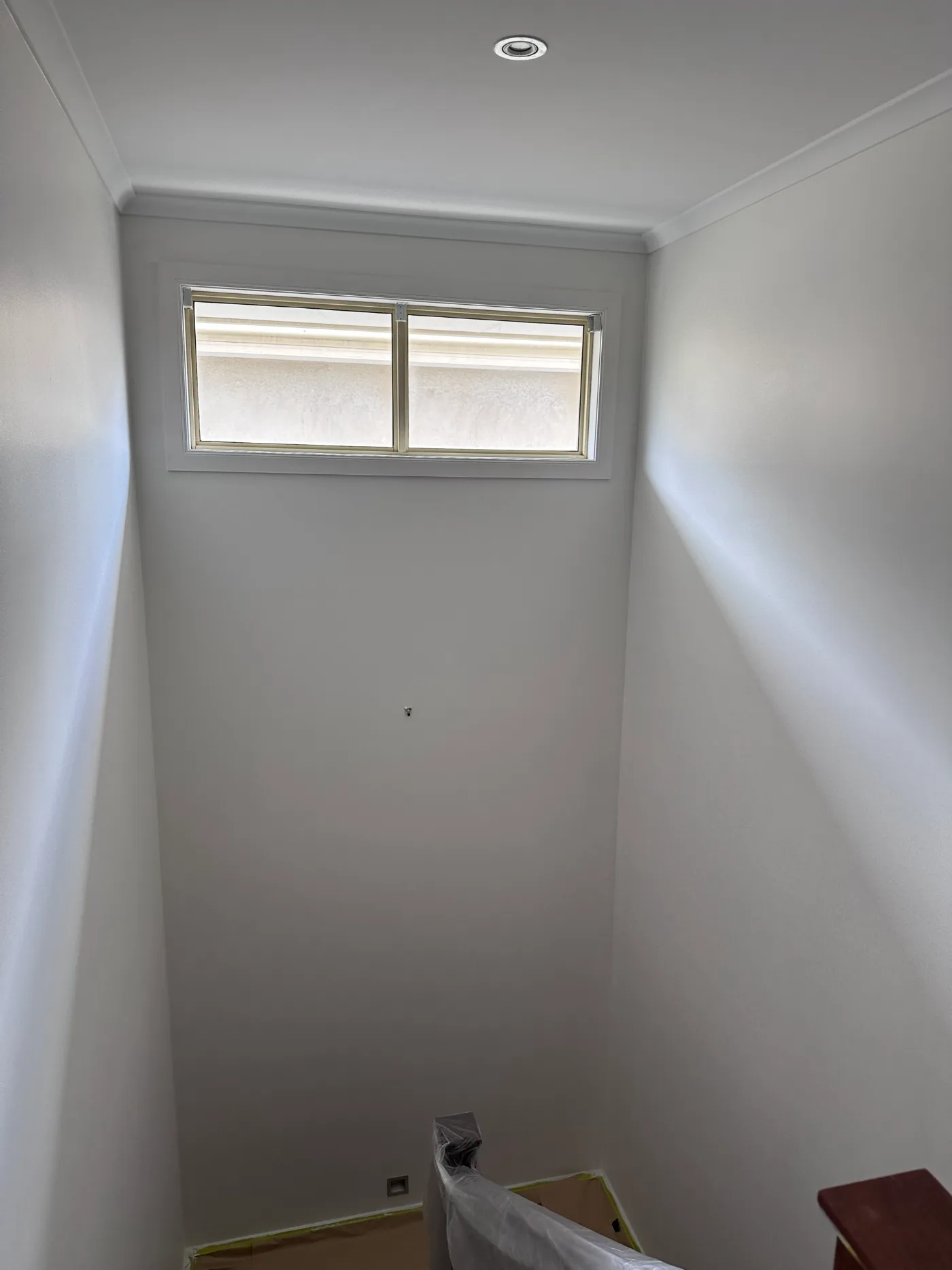 Stairwell wall in a Sandringham home after repainting, in a cool off-white with a white-framed window and cornice above the stairs
