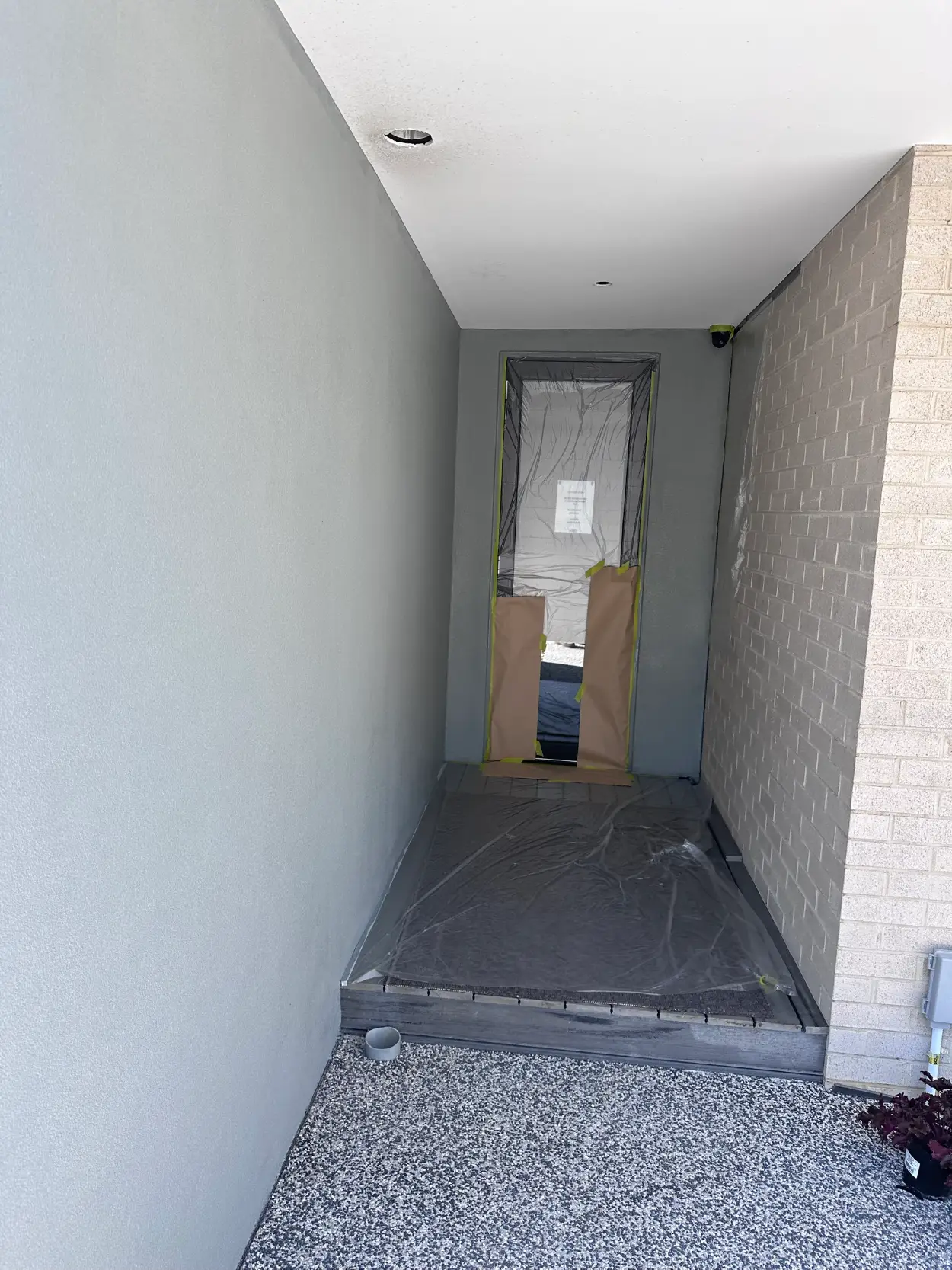 Entry alcove of a new Seaford townhouse during painting, the doorway wrapped in plastic and paper with the floor sheeted and the render coated in grey
