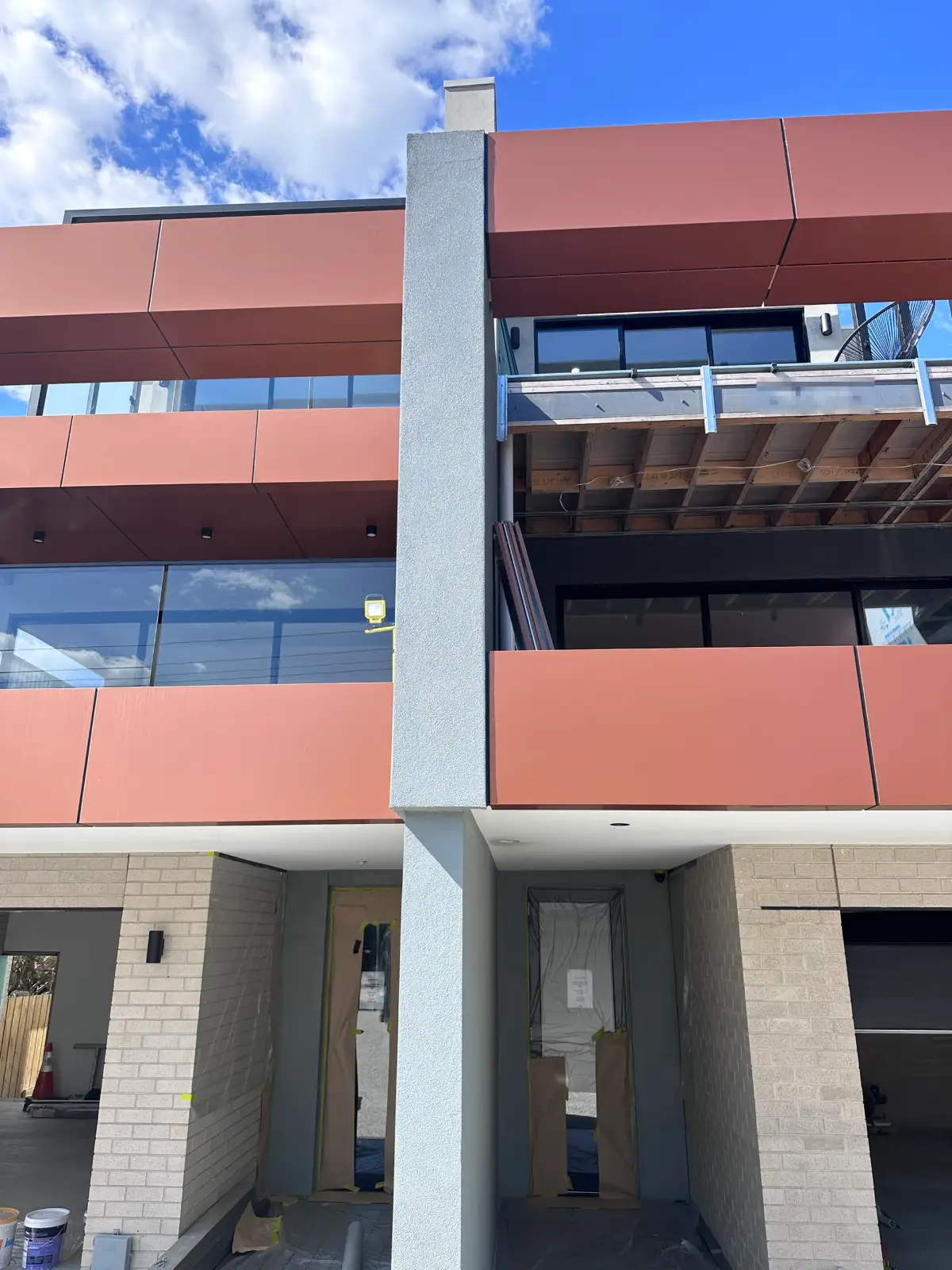 Street elevation of new Seaford townhouses during painting, with rendered grey columns running between terracotta composite panels and masked entries below