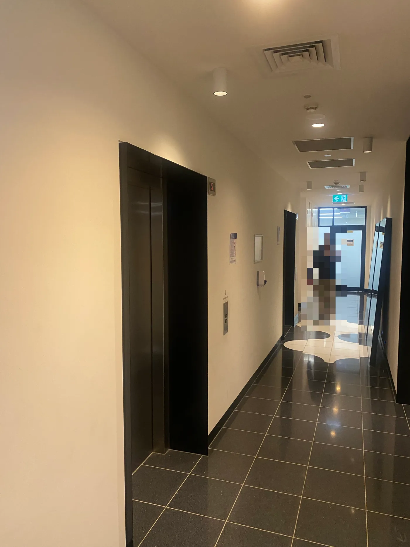 Lift lobby and corridor in a South Yarra apartment building after repainting, with white walls and ceiling, dark polished floor tiles and recessed downlighting