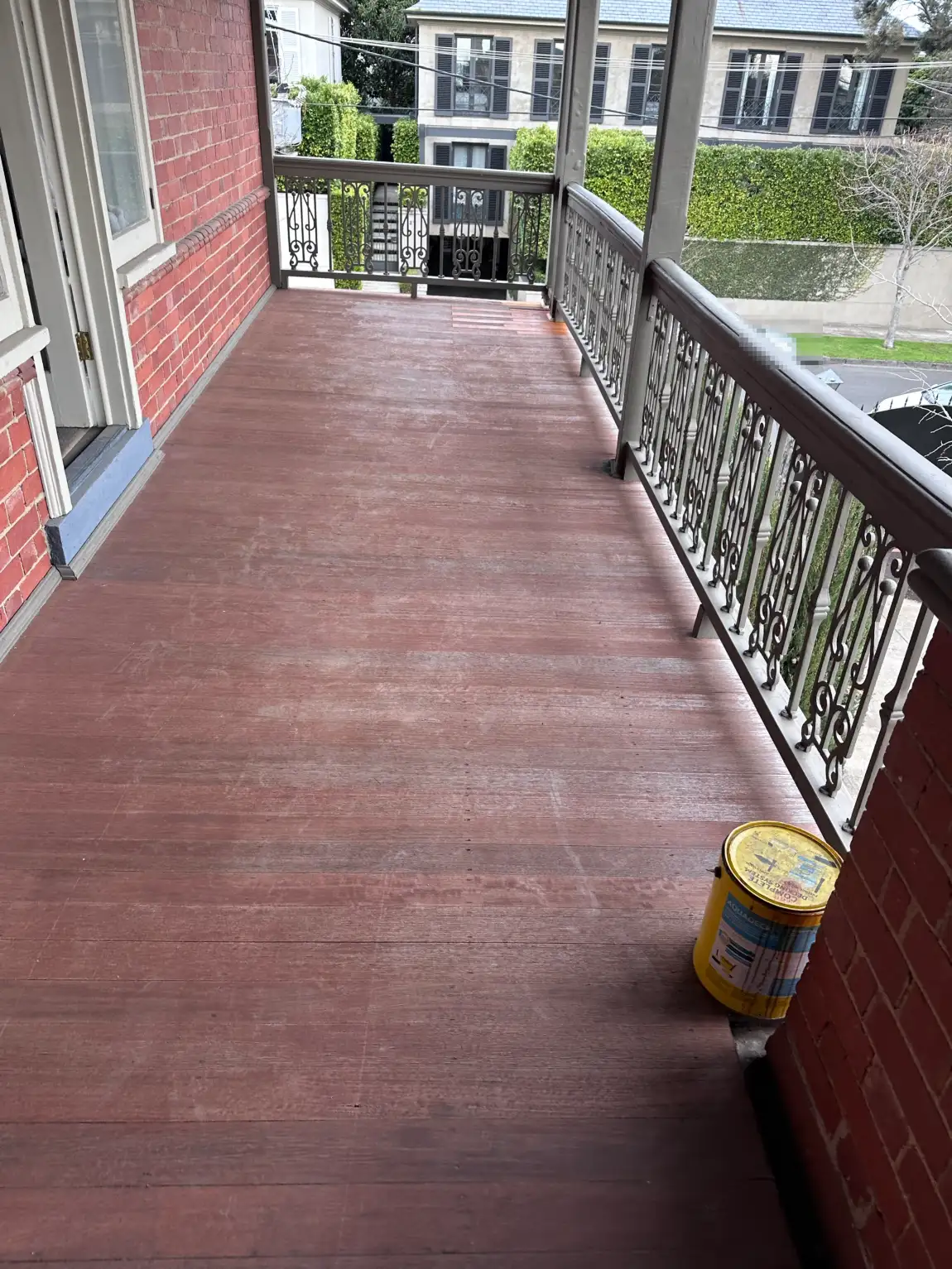 Full length of a recoated timber balcony on a period Stonnington home, running between the red brick wall and the cast-iron balustrade