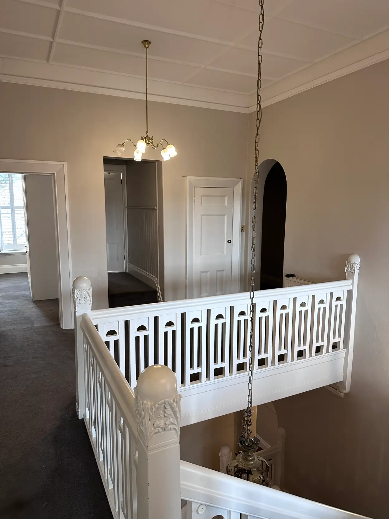 Stair landing in a period Stonnington home after repainting, with a white balustrade of cut-out fretwork panels, carved newel capitals and a battened ceiling above soft beige walls