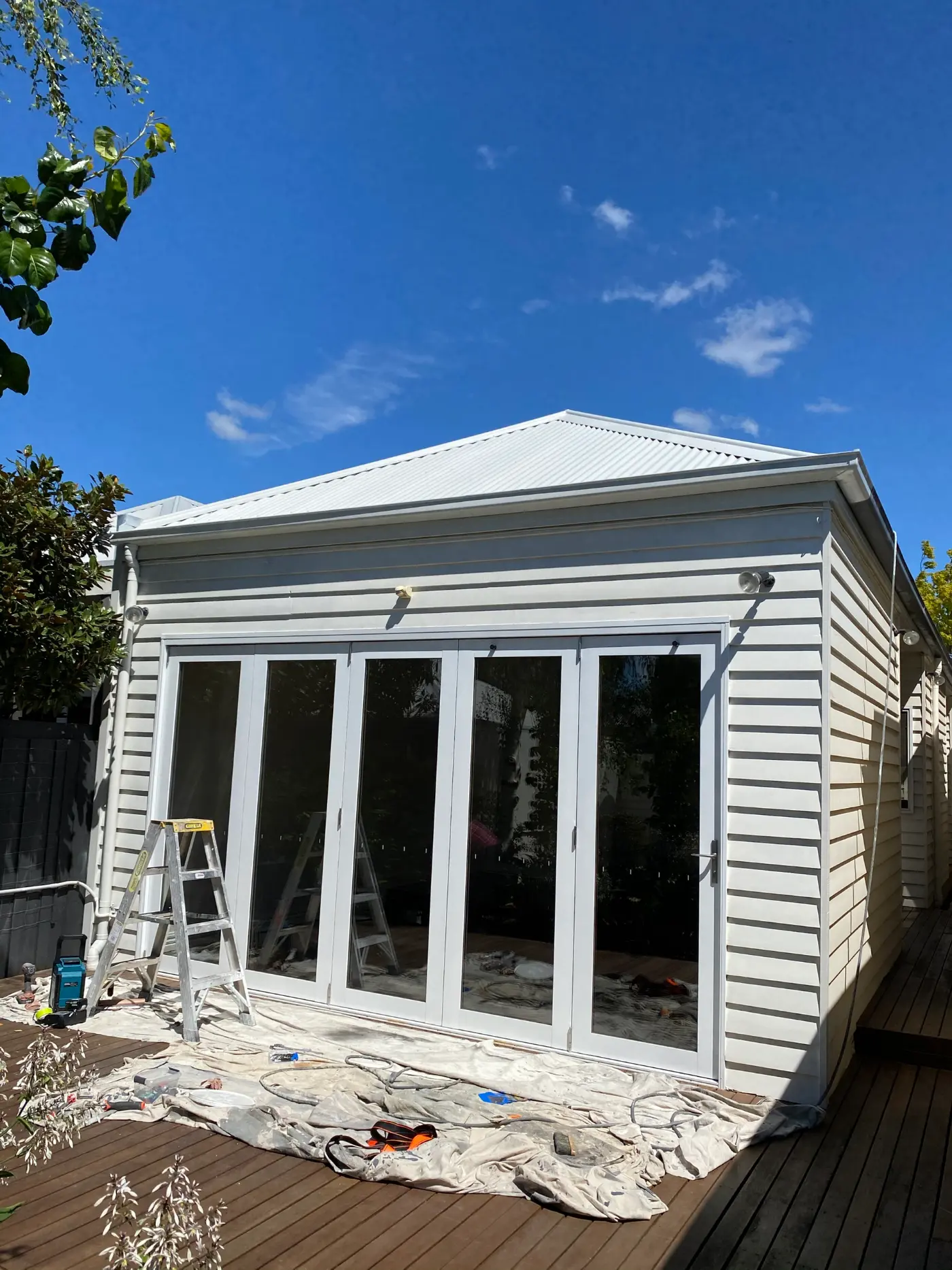 Rear weatherboard extension of a Toorak home after exterior painting, with white cladding, fascia and a run of timber bifold doors opening onto a timber deck