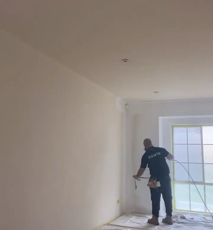 A Jetblack painter spraying the walls of an empty room in Wantirna South, with the window taped and masked and the floor sheeted