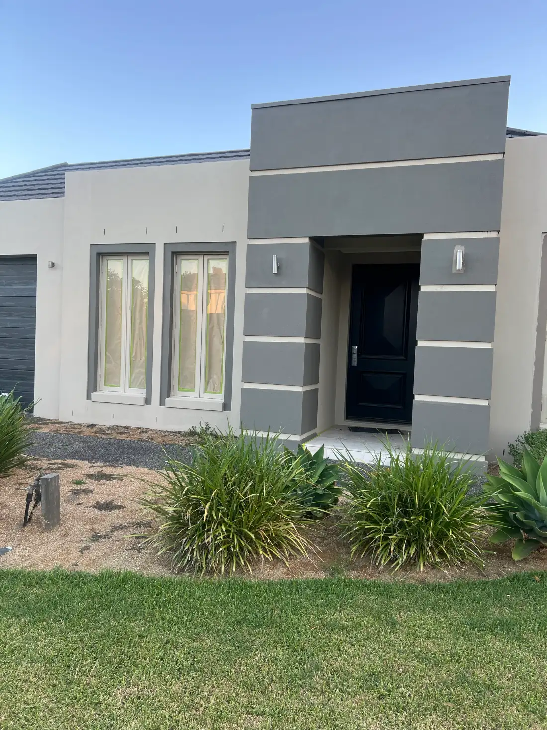Rendered entry elevation of a Waterways home during painting, in two tones of grey with the windows taped and papered off either side of a black front door